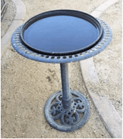 Metal birdbath on sandy ground.