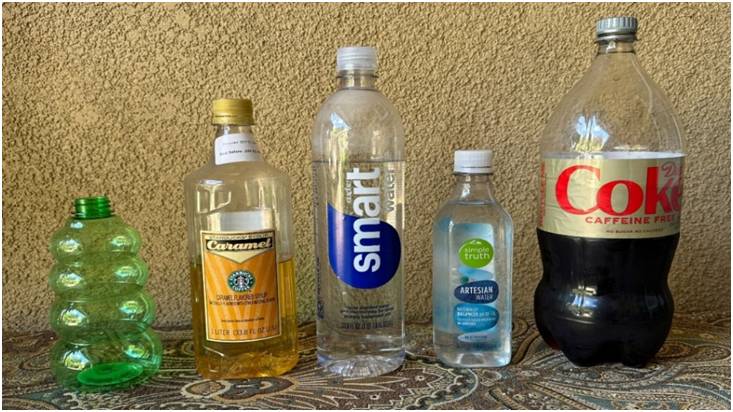 Four bottles with different beverages arranged on a table against a beige wall.