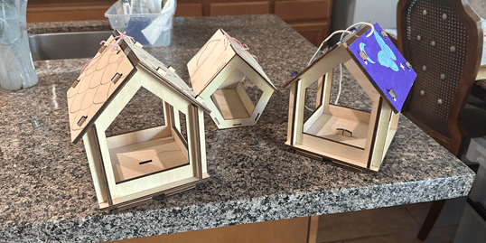 Three handcrafted wooden birdhouses with varied roof designs on a kitchen counter.